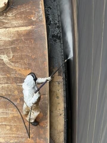 Operator in protective PPE hydro-blasting a rusted surface